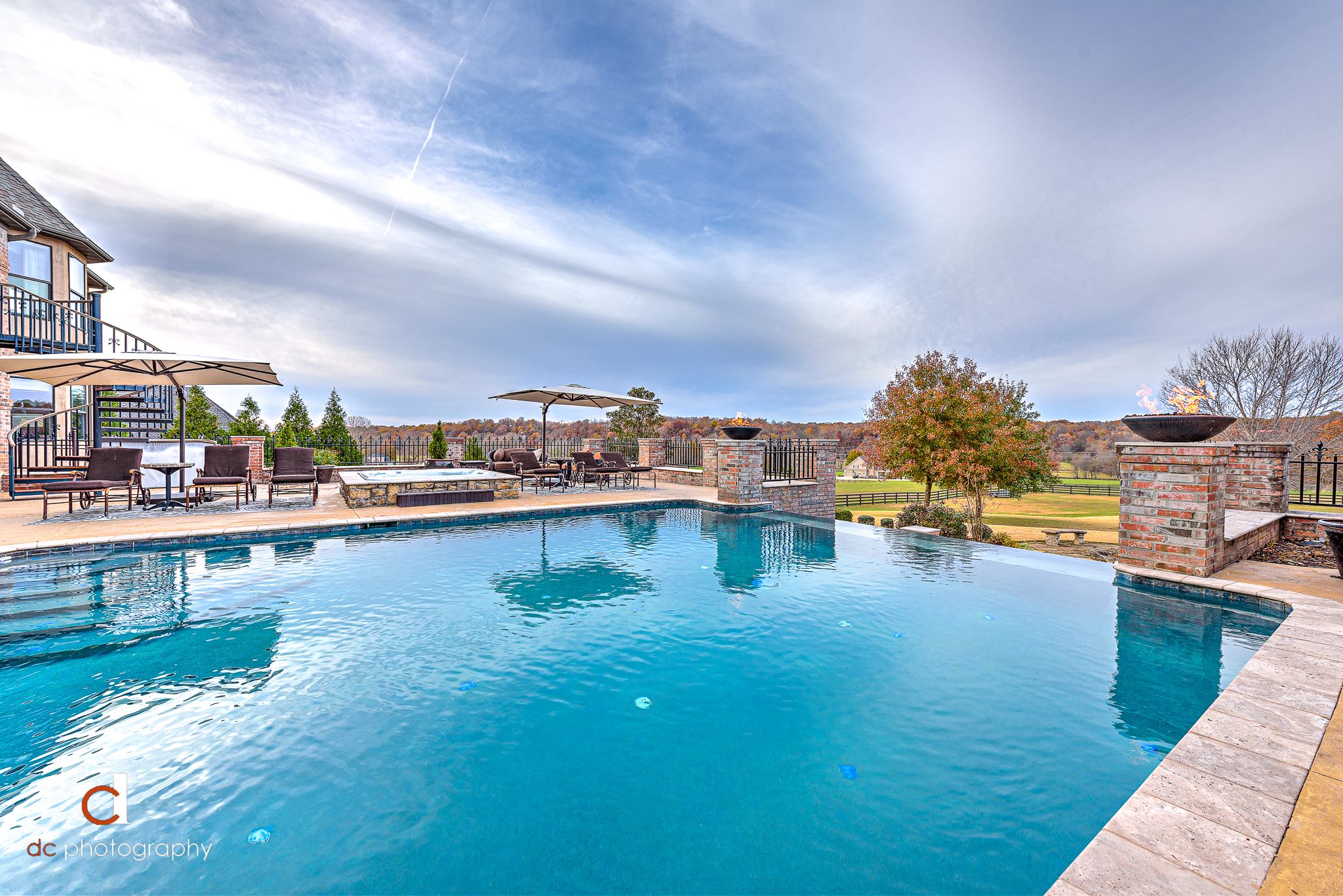 Vanishing-edge gunite pool with brick fire-bowl columns and patio overlooking open countryside