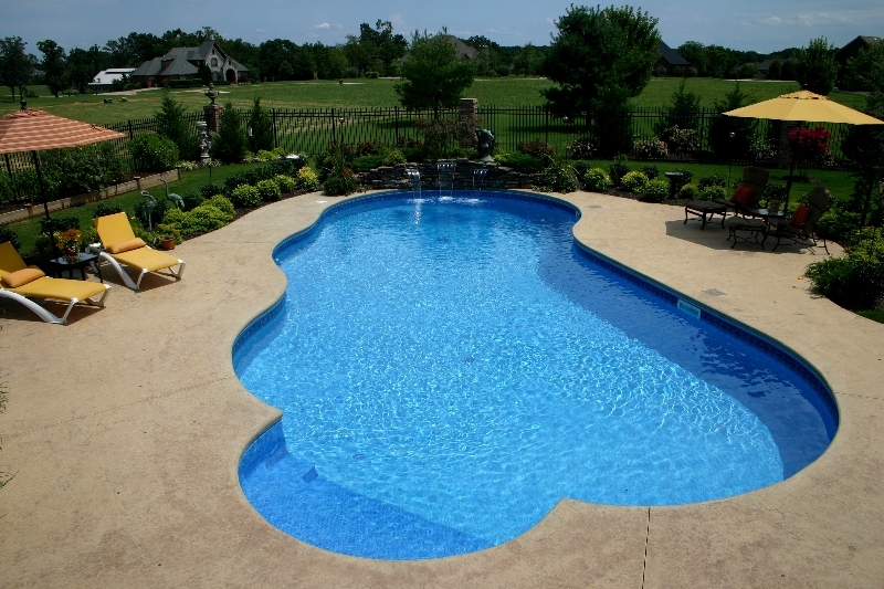 Freeform inground pool with rock waterfall, stamped concrete deck, and yellow lounge chairs