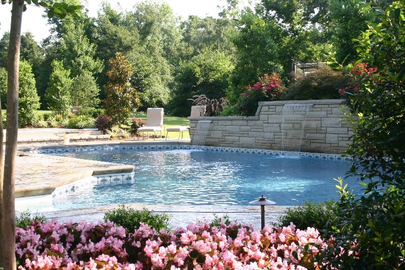 Gunite pool with tile border and stone wall sheer waterfalls framed by pink flowers