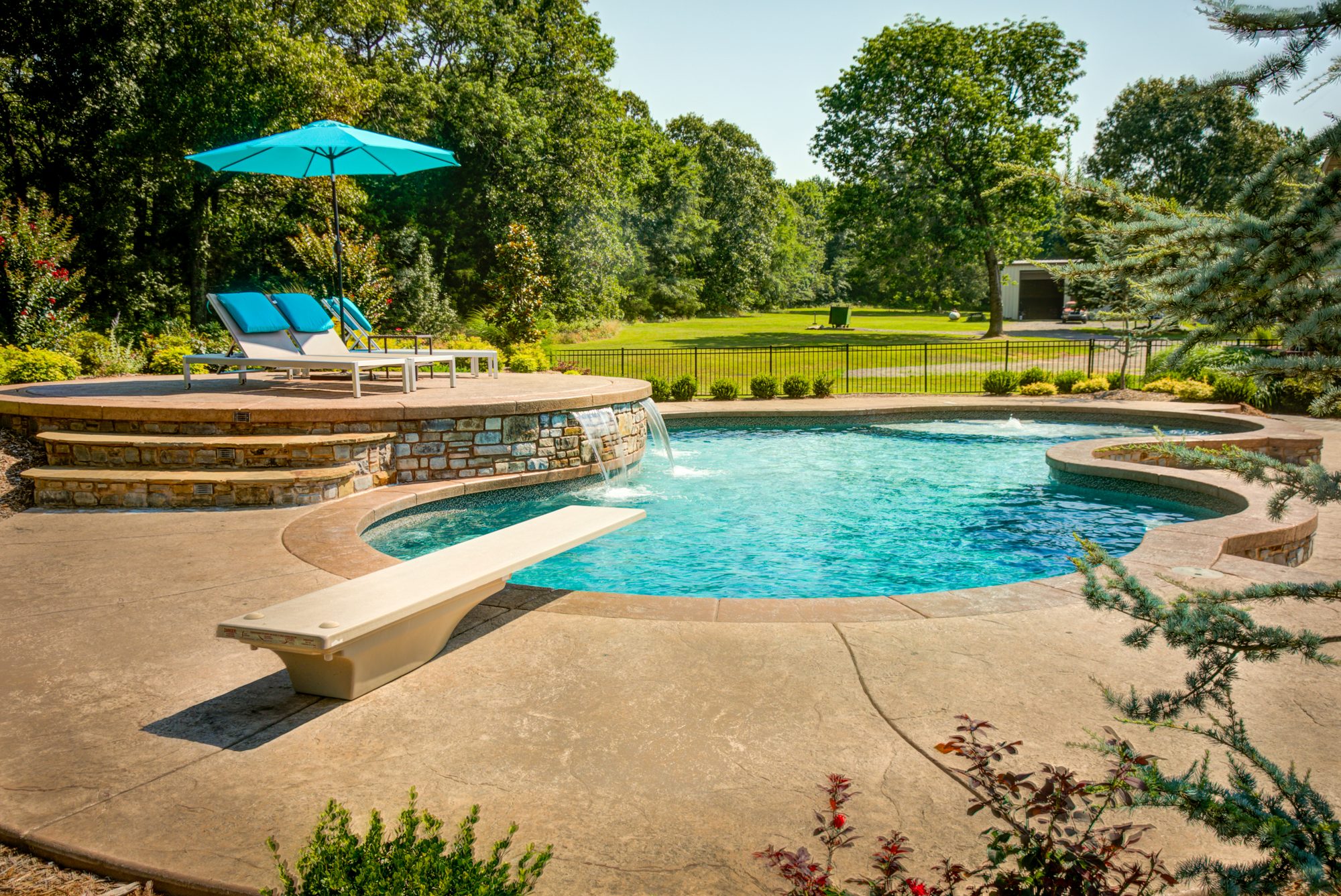 Freeform gunite pool with diving board, raised stone sun deck, and waterfall spillovers